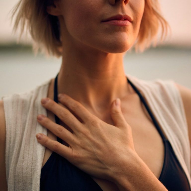 Frau mit kurzem Haar, die lässig ihr Herz hält, im Hintergrund unscharfer Wasserblick.