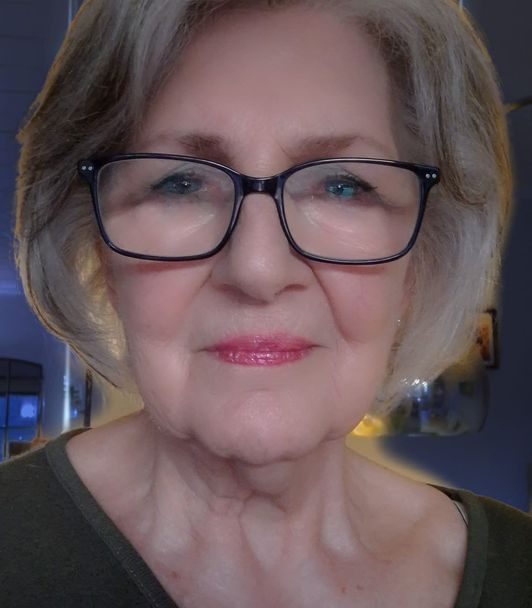 Ältere Frau ( Hanne-Lore Neumüller) mit Brille und kurzen, grauen Haaren lächelt freundlich in die Kamera.